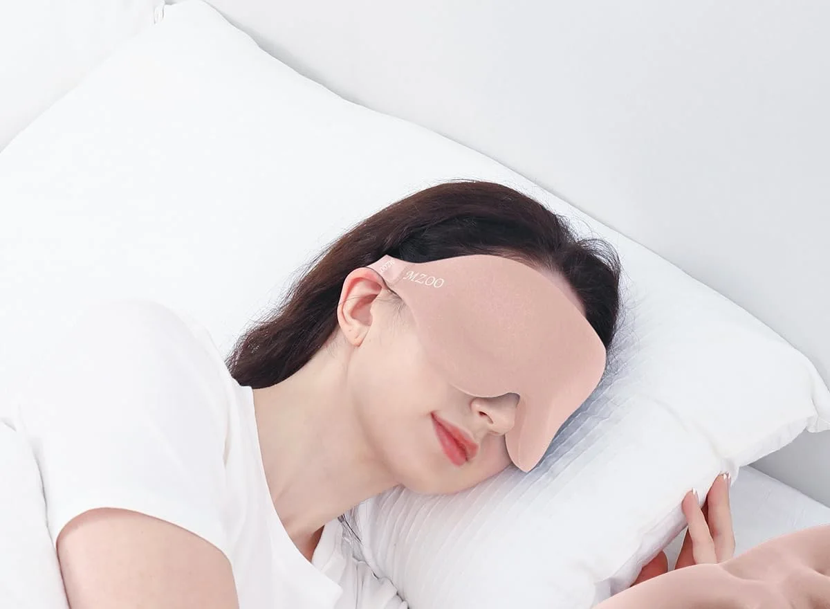 A side sleeper on her pillow in a pink MZOO Contoured mask, the strap running above her ear.